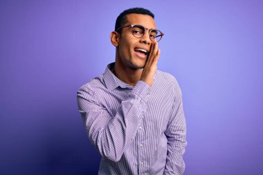 Yakışıklı afro-amerikan adam çizgili gömlek ve gözlük takıyor mor arka planda el ağızda gizli dedikodular söylüyor, kötü niyetli konuşmalar fısıldıyor