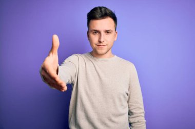Mor izole edilmiş arka planda günlük süveter giyen yakışıklı beyaz bir adam dostça bir selamlama ve hoş geldin hediyesi olarak el sıkışma sunuyor. Başarılı bir iş..