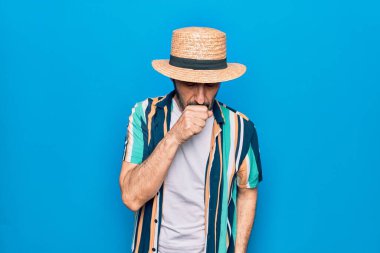 Mavi arka planda tişört ve şapka takan orta yaşlı yakışıklı turist kendini iyi hissetmiyor ve soğuk algınlığı veya bronşitin belirtisi olarak öksürüyor. Sağlık hizmeti kavramı.