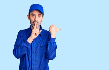 Tamirci üniforması giyen orta yaşlı yakışıklı adam sessiz olmak istiyor. Parmakları dudaklarında, elleri yandan işaret ediyor. sessizlik ve gizli konsept. 