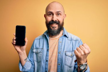 Sakallı yakışıklı kel adam sarı arka planda ekranda gururla bağırıyor ve zaferi ve başarıyı kutluyor.