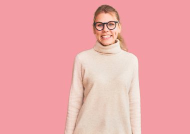 Güzel sarışın kadın balıkçı yaka kazak giyiyor ve yüzünde mutlu ve havalı bir gülümseme olan gözlük takıyor. şanslı kişi. 