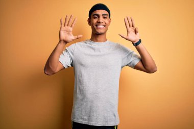 Yakışıklı Afro-Amerikan sporcu sarı arka planda spor giysisi giyiyor ve dokuz numarayı gösterirken kendine güvenen ve mutlu gülümseyen..