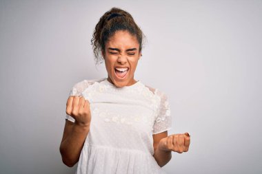 Genç ve güzel Afro-Amerikan kızı beyaz arka planda dikilmiş kolları havada ve gözleri kapalı bir şekilde başarıyı kutluyor ve şaşırıyor. Kazanan konsept.