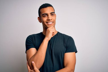 Beyaz arka plan üzerinde sıradan tişörtler giyen genç ve yakışıklı Afro-Amerikalı adam kameraya kollarını kavuşturmuş ve çenesini kaldırarak gülümsüyor. Olumlu düşünüyorum..