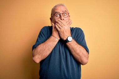 Sarı arka plan üzerine gündelik polo ve gözlük takan orta yaşlı, beyaz, yakışıklı bir adam ağzını yanlışlıkla ellerle kapatarak şok etti. Gizli konsept.