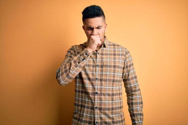 İzole edilmiş sarı arka plan üzerinde dikilen genç ve yakışıklı bir adam kendini iyi hissetmiyor ve soğuk algınlığı veya bronşitin belirtisi olarak öksürüyor. Sağlık hizmeti kavramı.