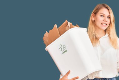 Geri dönüşüm kâğıdı kutusunu tutan genç, güzel sarışın kadın gülümsüyor. 