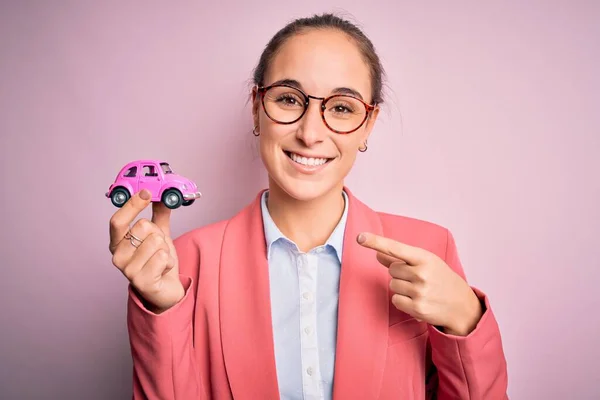 Νεαρή Όμορφη Επιχειρηματίας Φορώντας Γυαλιά Κρατώντας Ροζ Αυτοκίνητο Παιχνίδι Απομονωμένη — Φωτογραφία Αρχείου