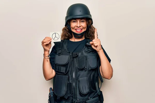 Middle age soldier woman wearing uniform and security helmet holding peace symbol reminder smiling with an idea or question pointing finger with happy face, number one