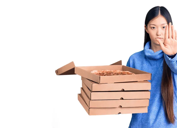 年轻美丽的中国女人拿着一盒纸盒意大利披萨 张开手做停止手势 表情严肃而自信 并摆出防守姿态 — 图库照片
