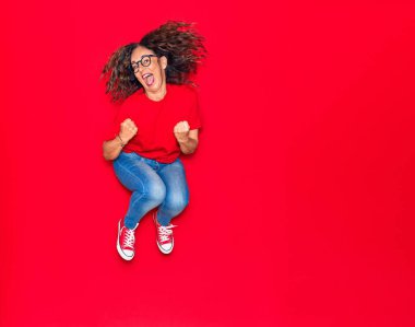 Orta yaşlı, güzel İspanyol bir kadın günlük kıyafetler ve mutlu bir gülümseme takınıyor. İzole edilmiş kırmızı arka planda yüzünde gülümsemeyle zıplıyor