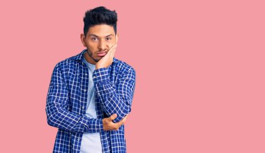 Yakışıklı Latin Amerikalı genç adam rahat tişört giyiyor. Kollarını kavuşturup depresyondan sıkılmış ve yorgun görünüyor.. 