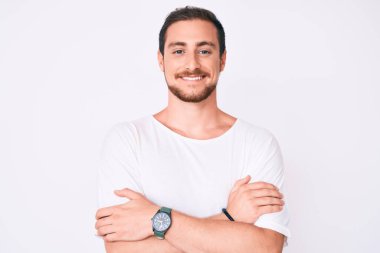 Sıradan beyaz tişört giyen, kolları çapraz gülümseyen ve kameraya bakan genç yakışıklı adam. pozitif kişi. 