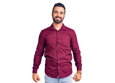 Gündelik kıyafetler giyen genç İspanyol adam pozitif ve mutlu görünüyor. Kendine güvenen bir gülümsemeyle ayakta duruyor ve dişlerini gösteriyor. 