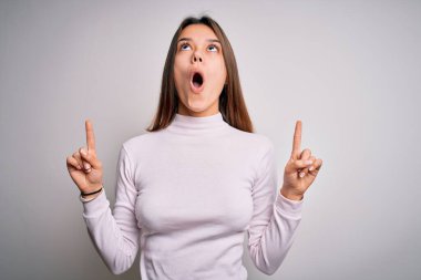 Genç ve güzel esmer kız, gündelik süveter giyiyor. İzole edilmiş beyaz arka plan üzerinde duruyordu. Şaşırmış ve şaşırmıştı..