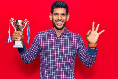 Genç latin adam kupayı tutuyor. Tamam imzasını atıyor. Parmaklarıyla imzalıyor. Gülümsüyor. 