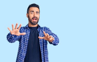 Günlük giysiler giyen genç İspanyol adam korku ifadesinden korkuyor ve dehşete düşüyor. El hareketlerini durdur, şok içinde bağır. panik konsepti. 