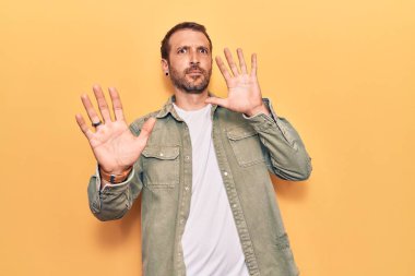 Sıradan kıyafetler giyen genç yakışıklı adam korku ifadesinden korkmuş ve dehşete düşmüş. El hareketlerini durdur, şok içinde bağır. panik konsepti. 