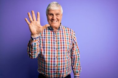 Kıdemli yakışıklı, beyaz gömlekli, soyutlanmış mor arkaplanlı, kendine güvenen ve mutlu gülümseyen, beş numaralı parmaklarıyla işaret eden adam..