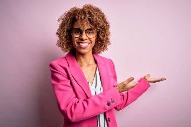 Pembe arka planda duran gözlüklü genç Afro-Amerikalı iş kadını gülümseyerek içeri girmeye davet ediyor.