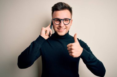 Yakışıklı, beyaz bir adam akıllı telefondan konuşuyor. Kocaman gülümsüyor, gülümsüyor. İşaret veriyor.