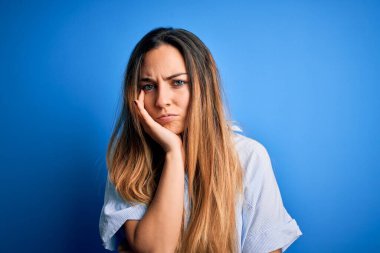 Mavi arka planda çizgili tişört giyen genç, güzel sarışın kadın kollarını kavuşturup depresyondan sıkılmış ve yorgun görünüyor..