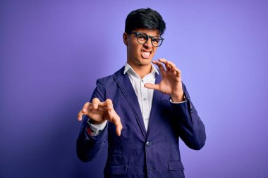 Ceket ve gözlük takan genç yakışıklı iş adamı mor arka planda komik bir şekilde gülüyor kedi gibi pençe hareketi yapıyor, agresif ve seksi bir ifade.