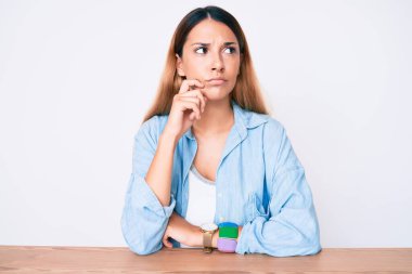 Genç esmer kadın gündelik giysiler içinde masada oturuyor ciddi bir yüz ifadesi var eli çenesinde soruyu düşünüyor, kafa karıştırıcı bir fikir hakkında düşünceli. 