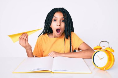 Elinde kağıt uçakla çalışan Afro-Amerikalı genç bir kız korkmuş ve ağzı açık bir şekilde şaşkınlık içinde çalışıyor. 