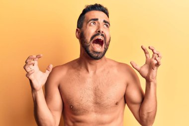 Genç İspanyol adam üstsüz, çılgın ve kızgın bir şekilde agresif bir ifadeyle bağırıyor ve kollarını kaldırıyor. hüsran kavramı. 