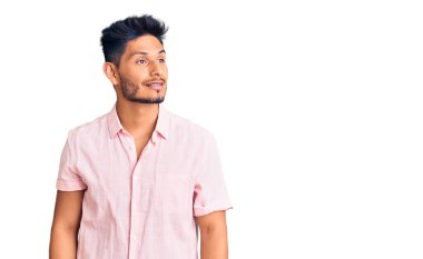 Yakışıklı Latin Amerikalı sıradan bir yaz tişörtü giymiş yüzünde gülümseme ve doğal bir ifadeyle yan yana bakan genç bir adam. Kendinden emin gülen. 