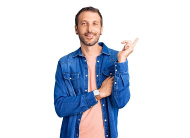 Yüzünde kocaman bir gülümseme olan sıradan kıyafetler giyen genç yakışıklı bir adam, kameraya el ve parmak ile bakıyor.. 