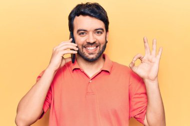 Genç İspanyol adam akıllı telefonda konuşuyor parmaklarıyla imza atıyor, gülümsüyor ve mükemmel bir sembol oluşturuyor. 