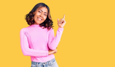 Genç, güzel, melez, pembe tişörtlü, gülümseyen, mutlu, eli ve parmağı yana doğru olan bir kadın. 