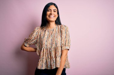 Moda kıyafetleri giyen genç ve güzel bir kadın. Manken, sokak tarzı giyiniyor. Pembe arka planda dikiliyor.