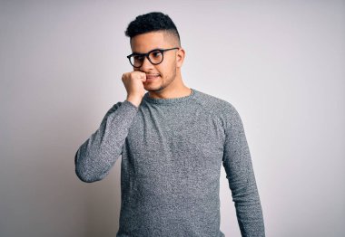 İzole edilmiş beyaz arka plan üzerinde gözlük takan genç yakışıklı bir adam elleri ağız yiyen tırnaklarla stresli ve gergin görünüyor. Endişe sorunu.