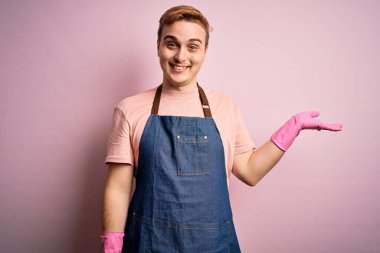 Genç, kızıl saçlı temizlikçi, önlük ve eldivenlerle ev işi yapıyor. Gülümsüyor, eli avucunda kameraya bakıyor..