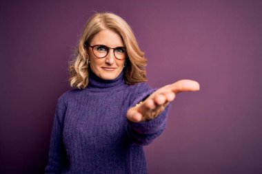 Orta yaşlı, sarışın, sıradan mor balıkçı yaka kazak giyen ve gözlüklü, dostça gülümseyerek el sıkışan hoş geldin diyen bir kadın. Başarılı bir iş..