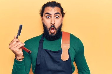 Önlük takan genç Arap adam berber ustura tutuyor. Şaşırtıcı bir şekilde ağzı açık kalmış, korkmuş ve şaşırmış. İnanmayan yüz. 