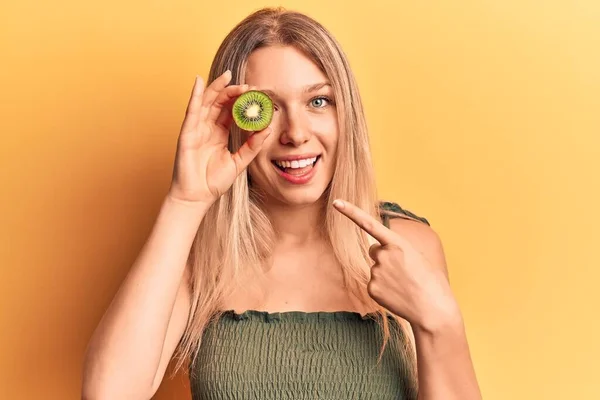Young Blonde Woman Holding Kiwi Smiling Happy Pointing Hand Finger — ストック写真