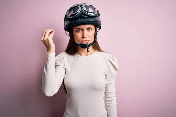 年轻美丽的骑摩托车的女人 蓝眼睛 戴着黑色的头盔 背景是粉红的 手指头自信地做着意大利手势 — 图库照片
