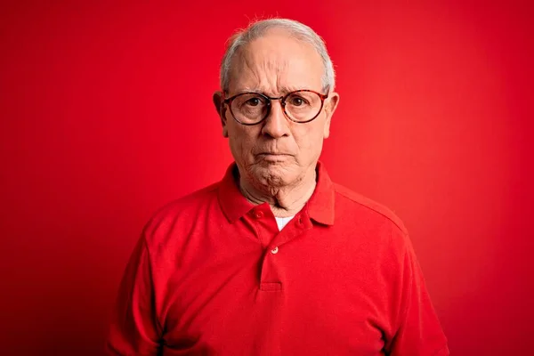 Grey haired senior man wearing glasses and casual t-shirt over red background skeptic and nervous, frowning upset because of problem. Negative person.