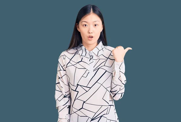 若い美しい中国人女性を着てカジュアルなシャツ驚きを指して手指で側に 口を開けて驚きの式 — ストック写真