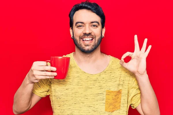 Joven Hombre Hispano Sosteniendo Café Haciendo Signo Con Los Dedos —  Fotos de Stock