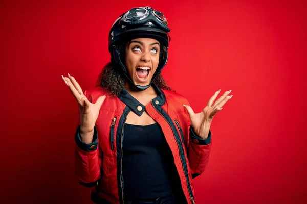 赤い背景の上に元ヘルメットと眼鏡を身に着けている若いアフリカ系アメリカ人のオートバイの女の子は狂気と怒鳴り 積極的な表現と腕を上げて叫んでいます 欲求不満の概念 — ストック写真