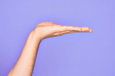 İzole edilmiş mor arka plan üzerinde parmaklarını gösteren beyaz bir gencin eli. Düz avuç içi ürünü sunuyor, el hareketi yapıyor, boş kopya alanı veriyor.