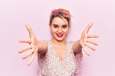 Genç, güzel, sarışın bir kadın sıradan kıyafetler giyip kameraya bakıyor. Sarılmak için kollarını açmış gülümsüyor. Mutluluğu kucaklayan neşeli bir ifade.. 