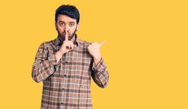 Gündelik giysiler giyen genç İspanyol adam sessiz olmak istiyor. Parmakları dudaklarında, elleri yandan işaret ediyor. sessizlik ve gizli konsept. 