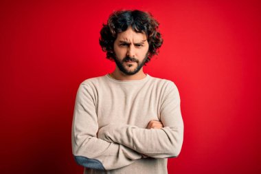 Sakallı, sıradan bir süveter giyen, kırmızı arka planda duran, kuşkucu ve gergin, yüzünde çapraz kollu tasvip etmeyen genç yakışıklı bir adam. Negatif kişi.
